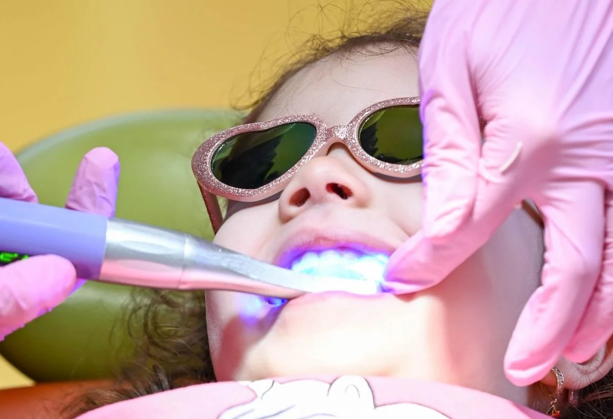 Fată mică cu ochelari, tratament dental cu lumină albastră.