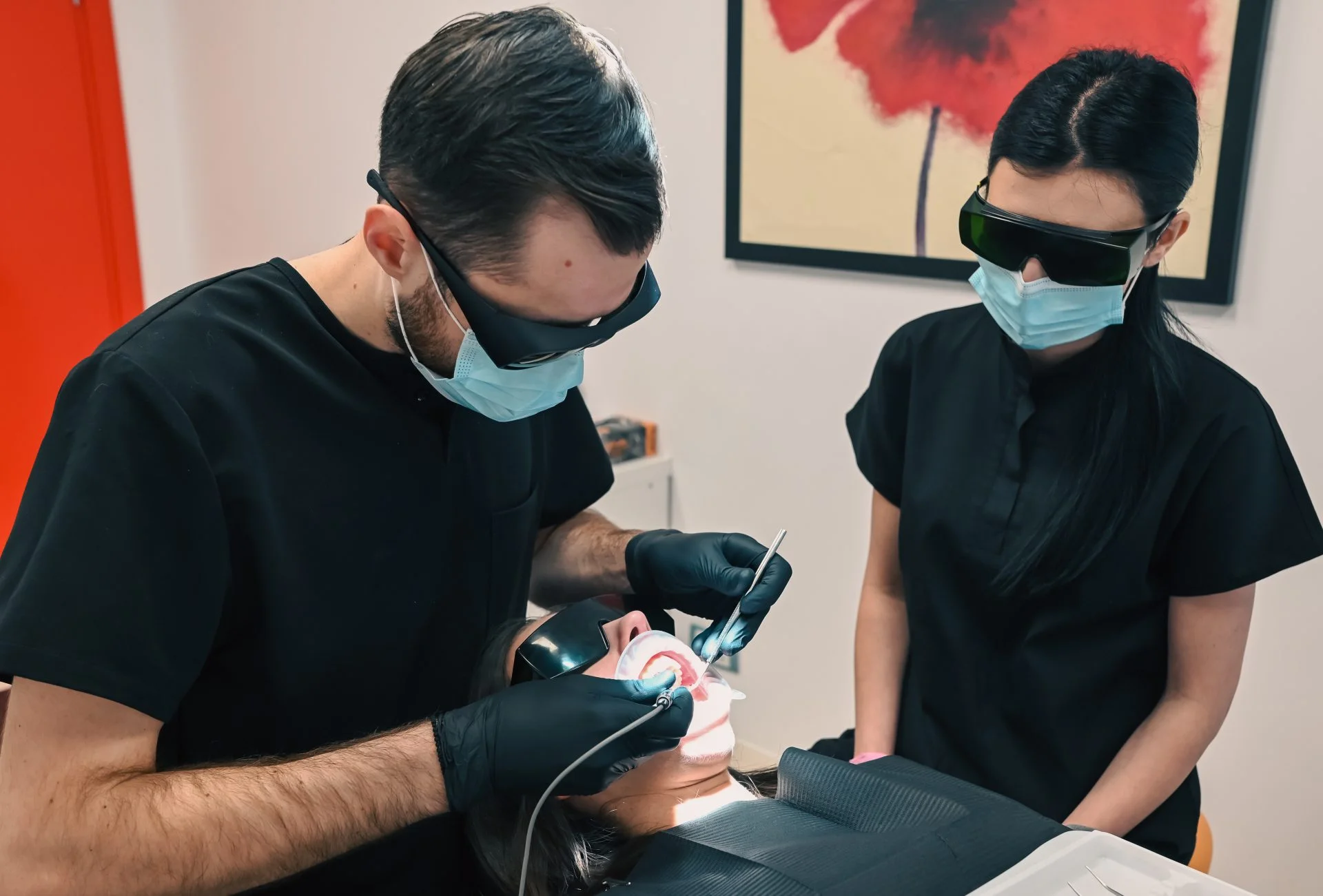 Dentist aplicând fațete dentare, purtând echipament de protecție negru.