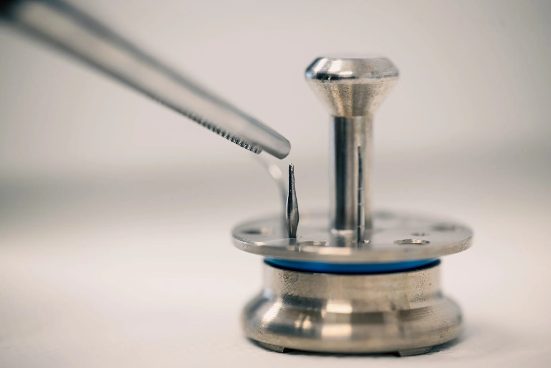 Instrument metalic dentar lângă suport circular, culoare argintie.