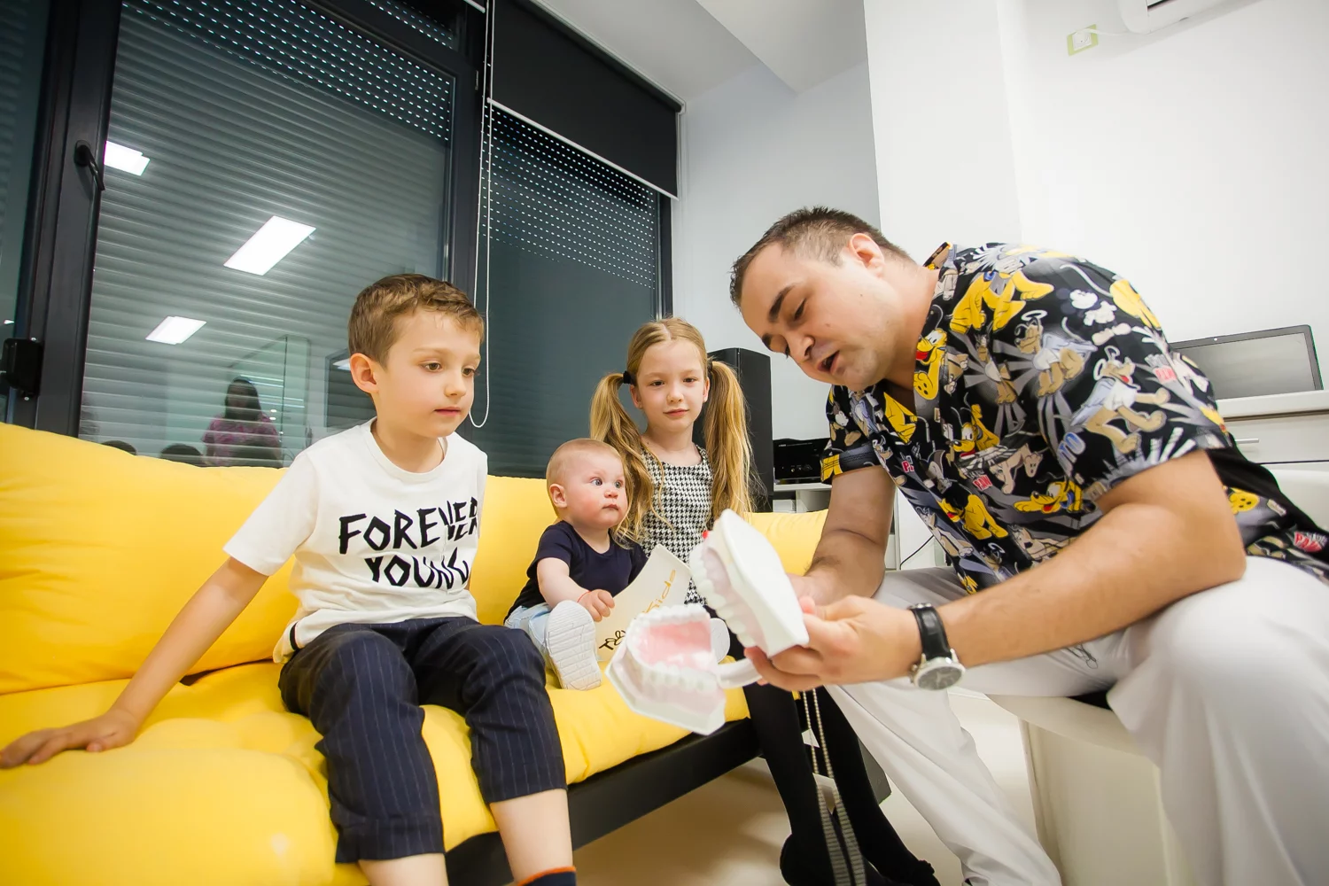 Trei copii pe canapea galbenă, adult cu model dentar.