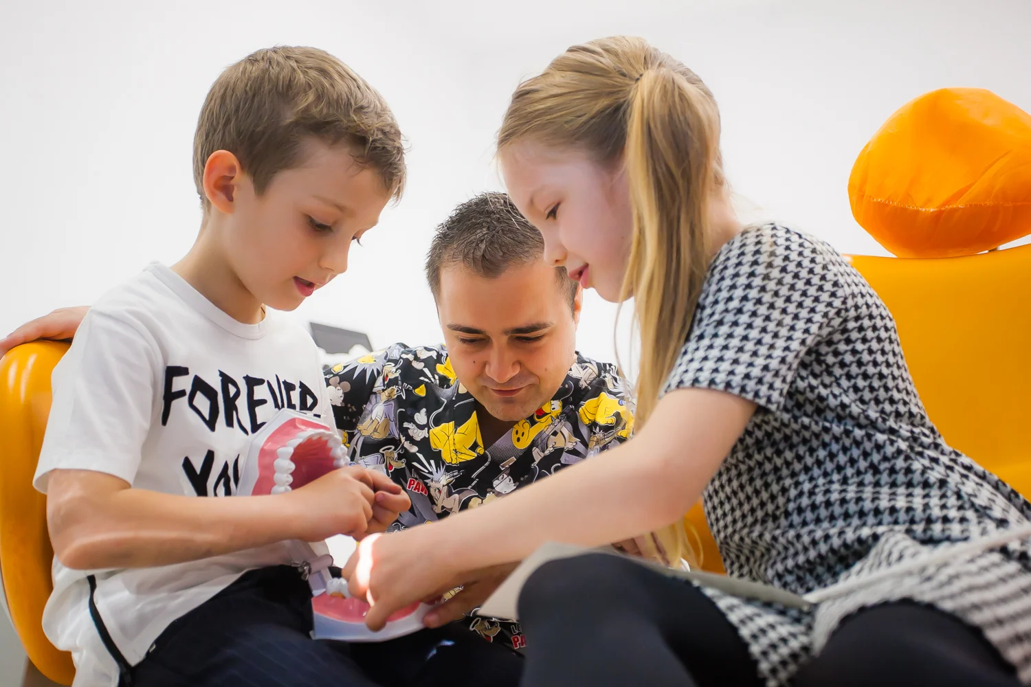 Doi copii și un adult observă un model dentar.