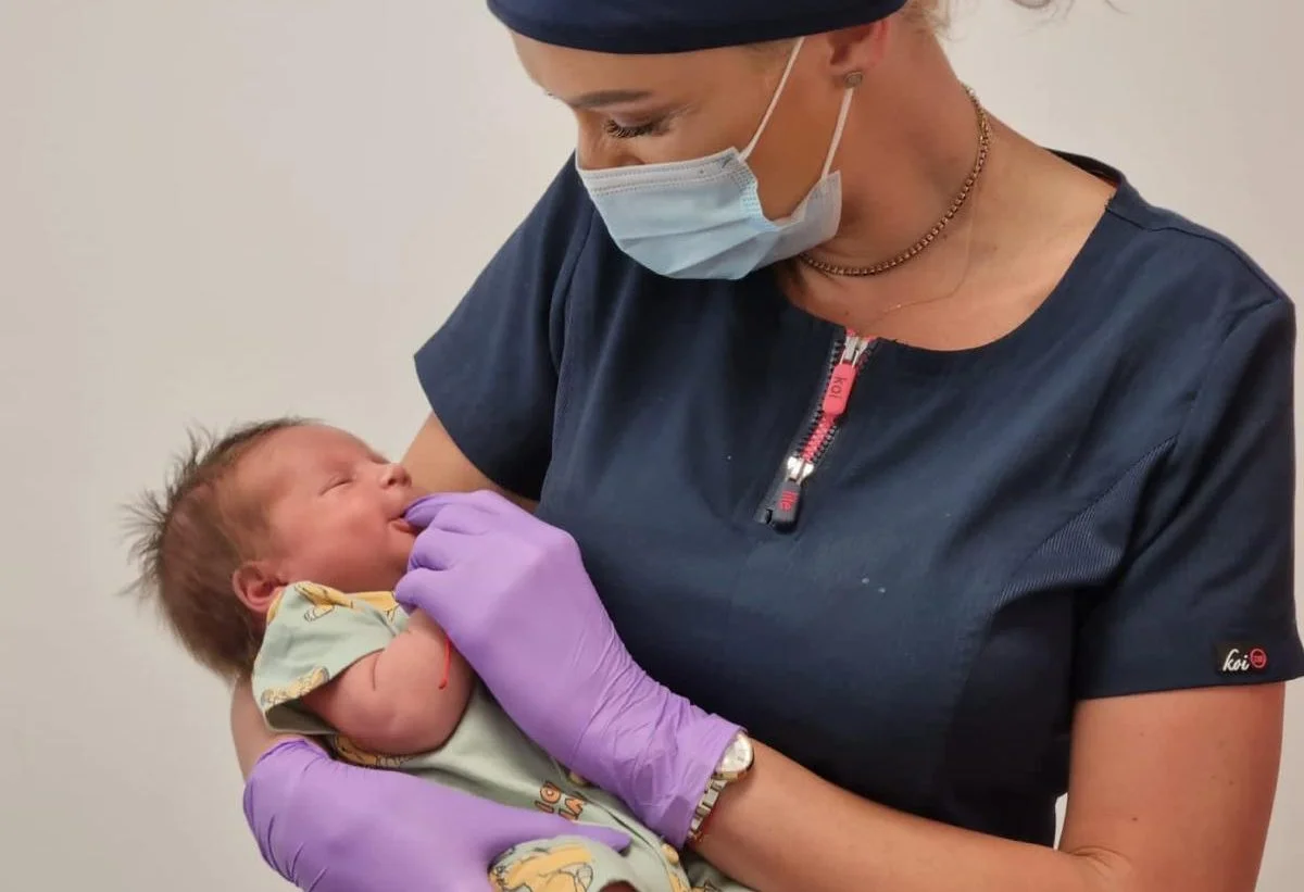 O persoană ține un nou-născut cu mănuși violet.